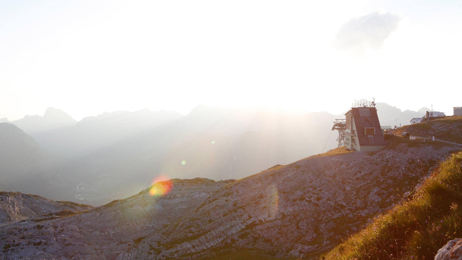 Sonnenuntergang in den Bergen mit Seilbahnstation auf felsigem Gipfel und Fernblick ins Tal.