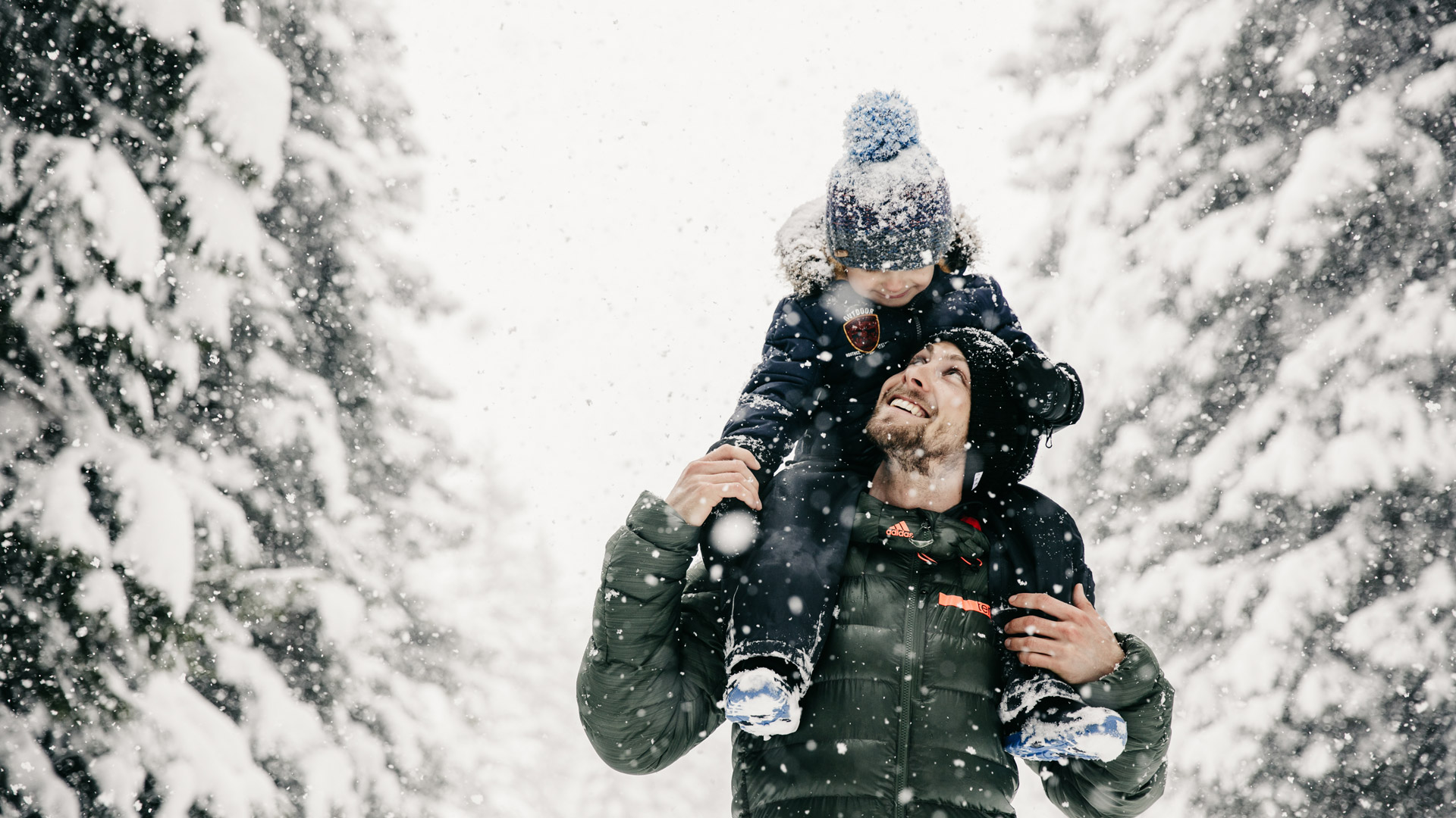 Mann mit Kind auf den Schultern bei Schneefall im Wald
